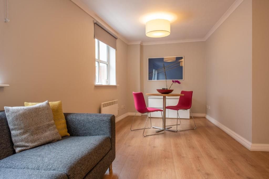 A modern living room with a grey sofa, two red chairs, a small table, and a painting on the wall.