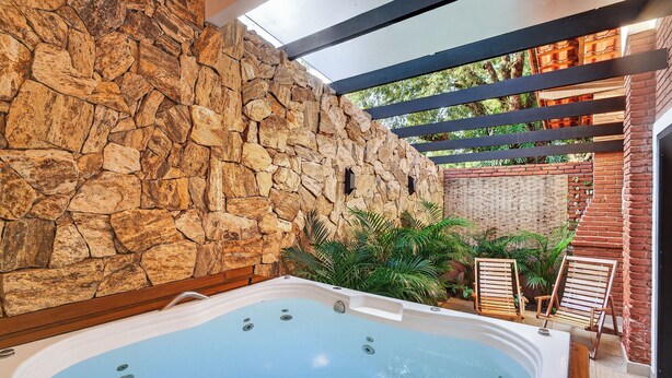 Un bain à remous avec un mur en pierre en arrière-plan, des sièges extérieurs et une vue sur la verdure.