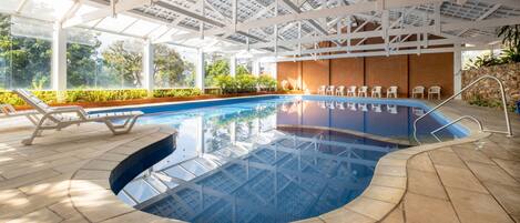 Una piscina techada, una piscina al aire libre, sombrillas