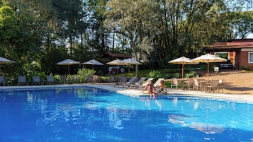 Una piscina techada, una piscina al aire libre, sombrillas