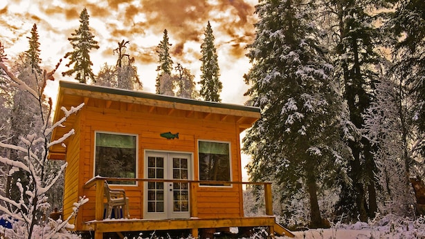 Uma cabana de madeira com varanda, rodeada por árvores cobertas de neve.
