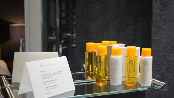 Une étagère en verre présente divers articles de toilette, et un panneau explicatif est placé à côté.