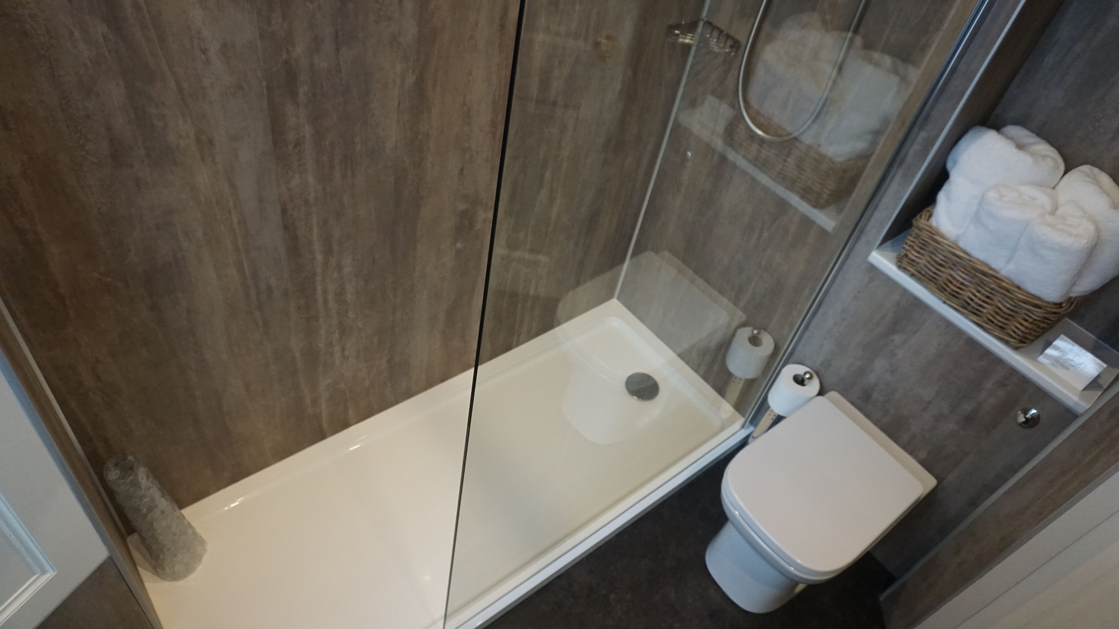 A modern bathroom with a glass-enclosed shower, a white toilet, and a shelf with towels.
