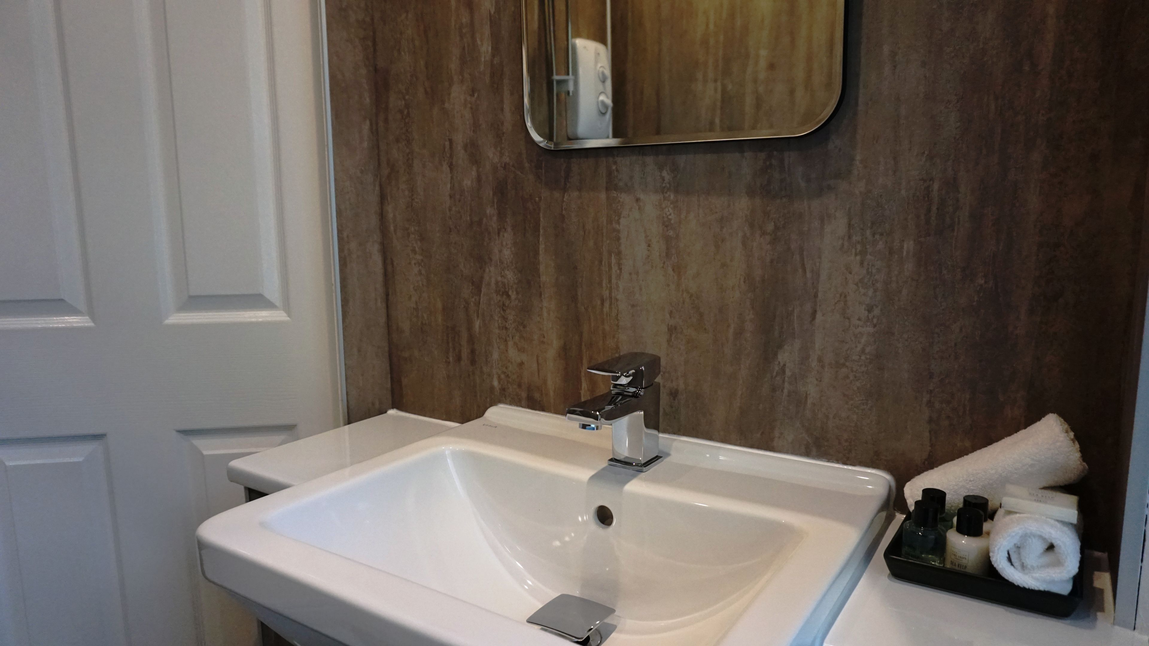 Un bagno con un lavandino bianco, uno specchio e articoli da toilette su un vassoio.