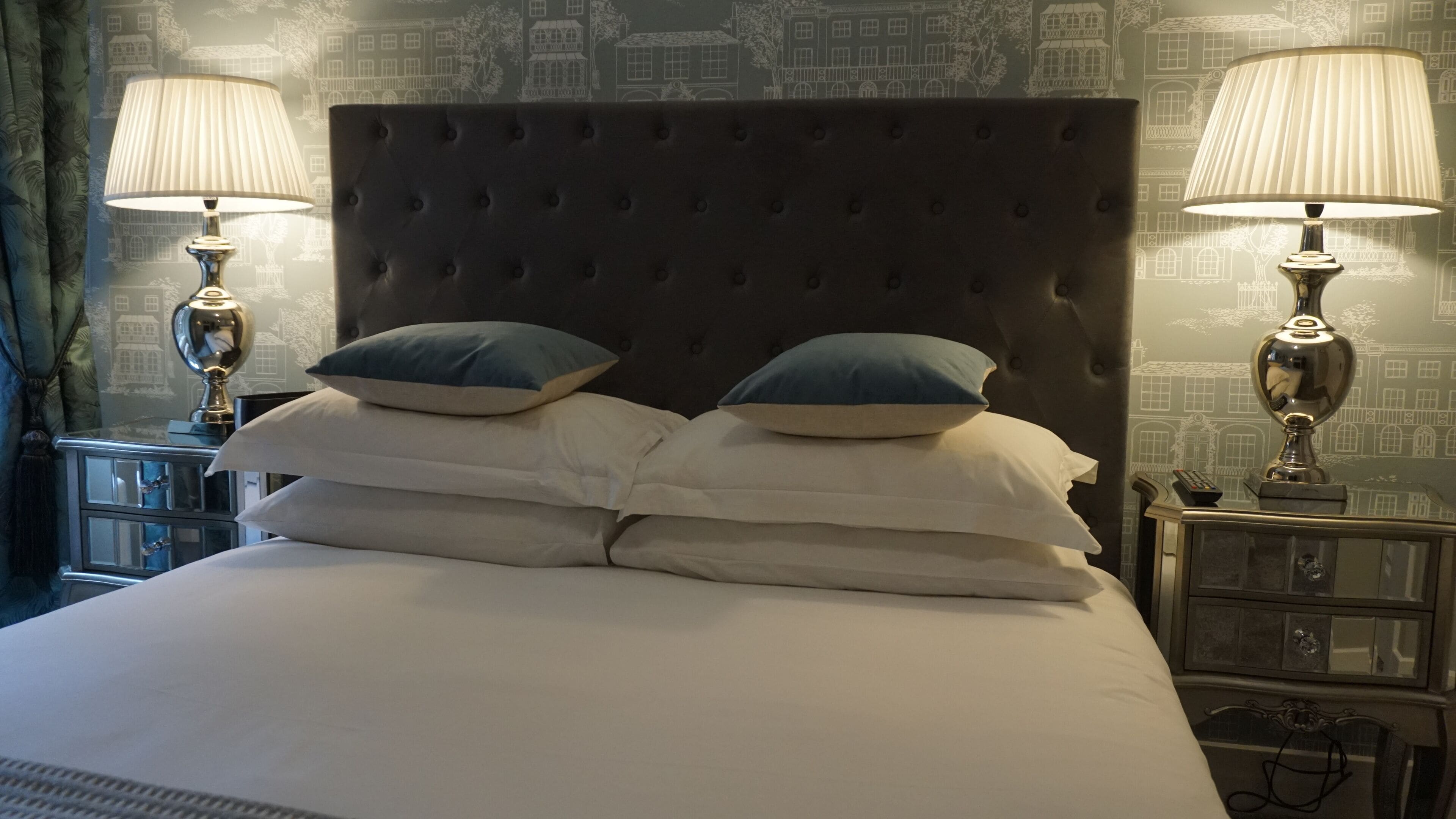 A neatly made bed with a tufted headboard, two bedside tables with lamps, and a patterned wallpaper.