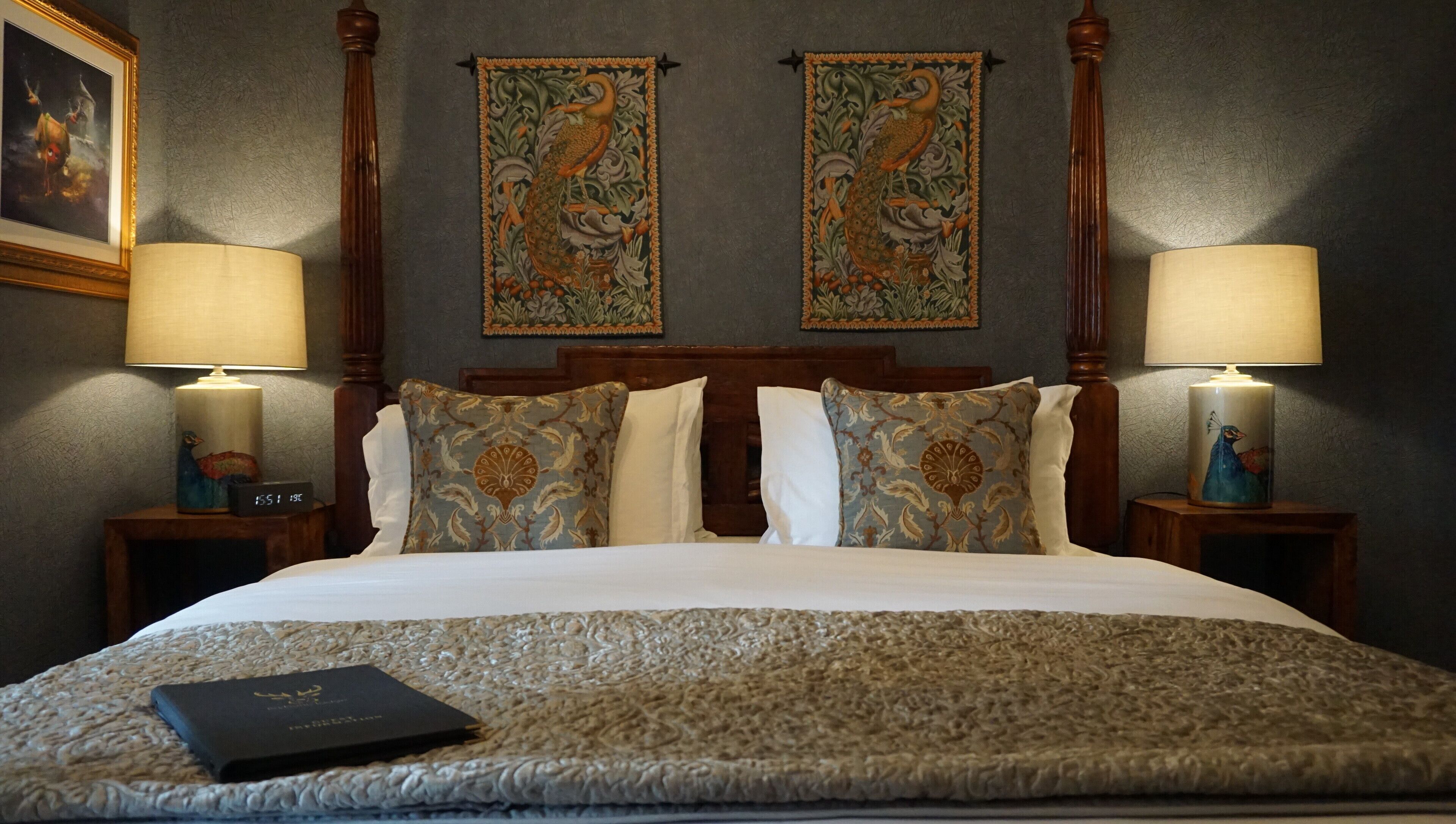 A neatly made bed with patterned pillows and a decorative throw, flanked by two wall-mounted lamps and a framed picture.