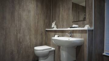 Un baño moderno con pared de madera, un inodoro blanco y un lavamanos blanco con un espejo encima.