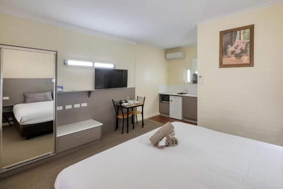 Ein Hotelzimmer mit einem Bett, einem Schreibtisch, einem Stuhl, einer kleinen Küchenzeile und einem Fernseher.