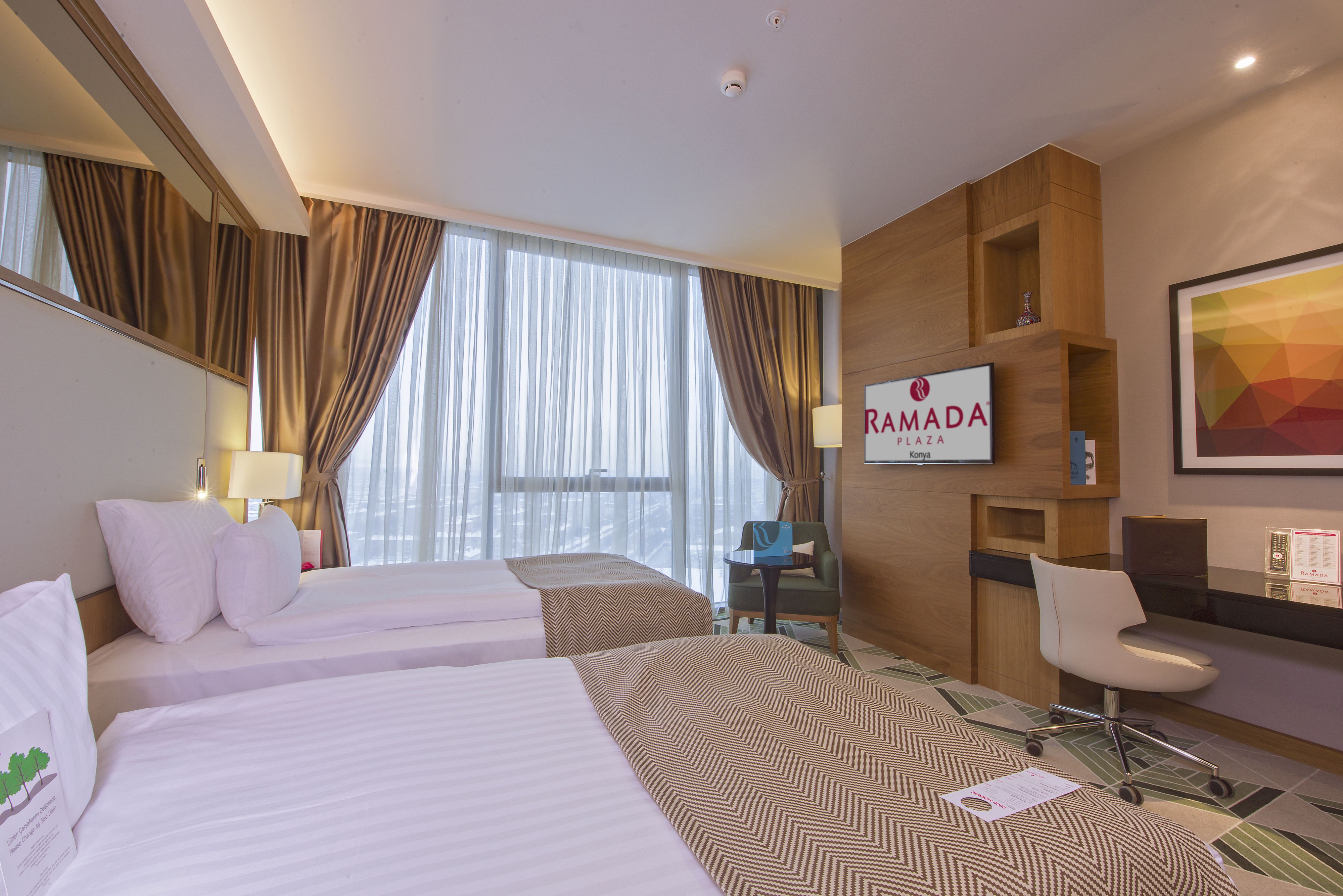 A hotel room with two beds, a desk, a chair, a TV, and a large window with curtains.