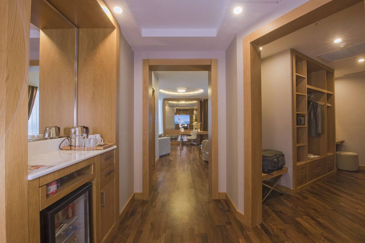 Un couloir d’hôtel avec un plancher en bois, une kitchenette, un coin salon et un téléviseur en arrière-plan.