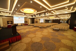 Un salón de conferencias con un escenario, un atril y una gran pantalla que muestra el logotipo de Ramada.