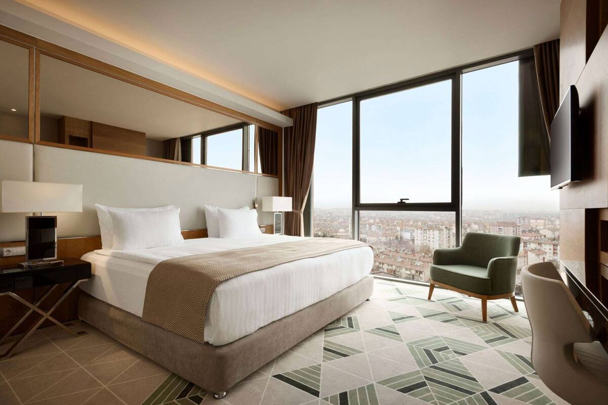 Une chambre d’hôtel avec un grand lit, une chaise, une télévision et une vue sur la ville.
