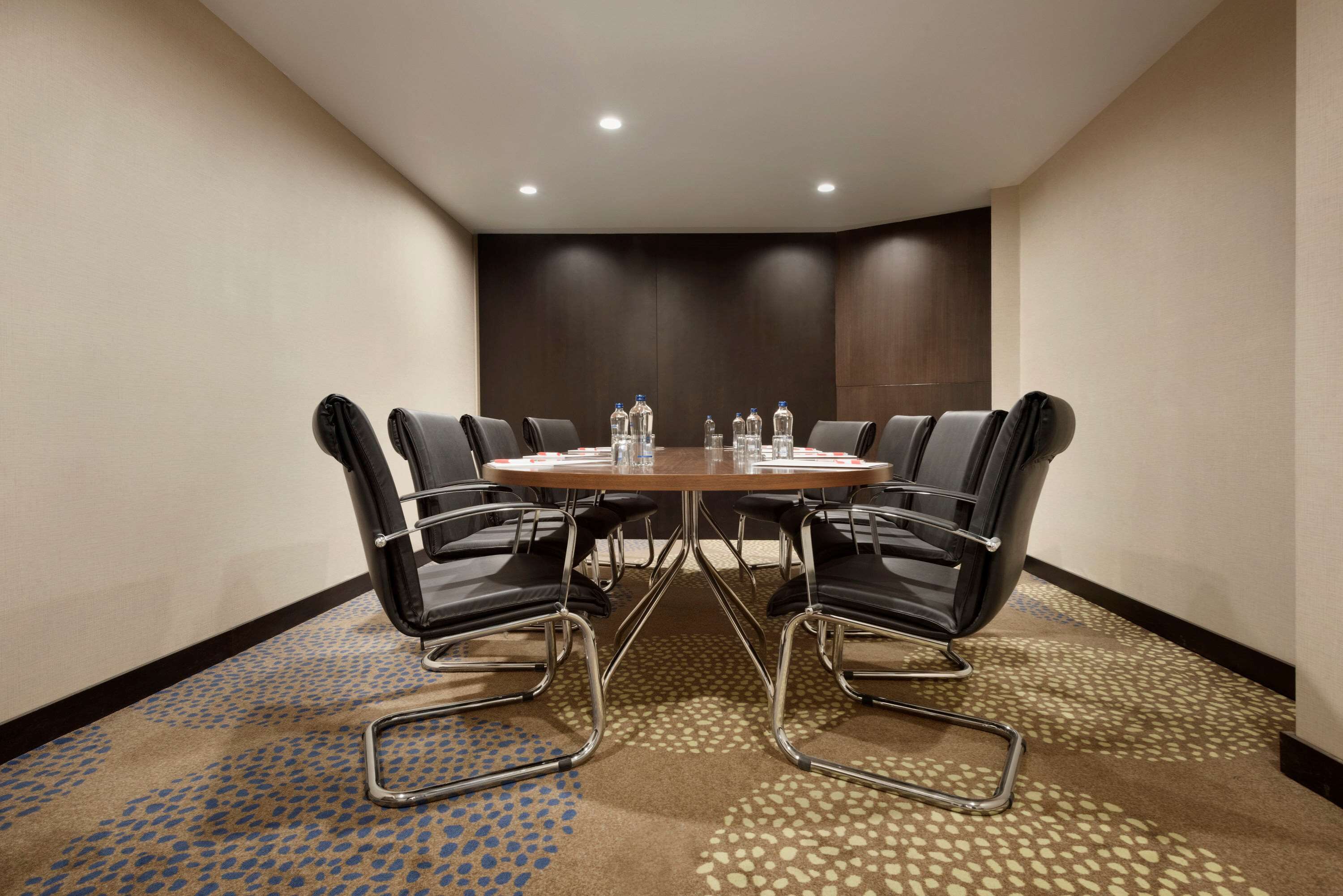 A conference room with a round table, eight black leather chairs, and water bottles on the table.