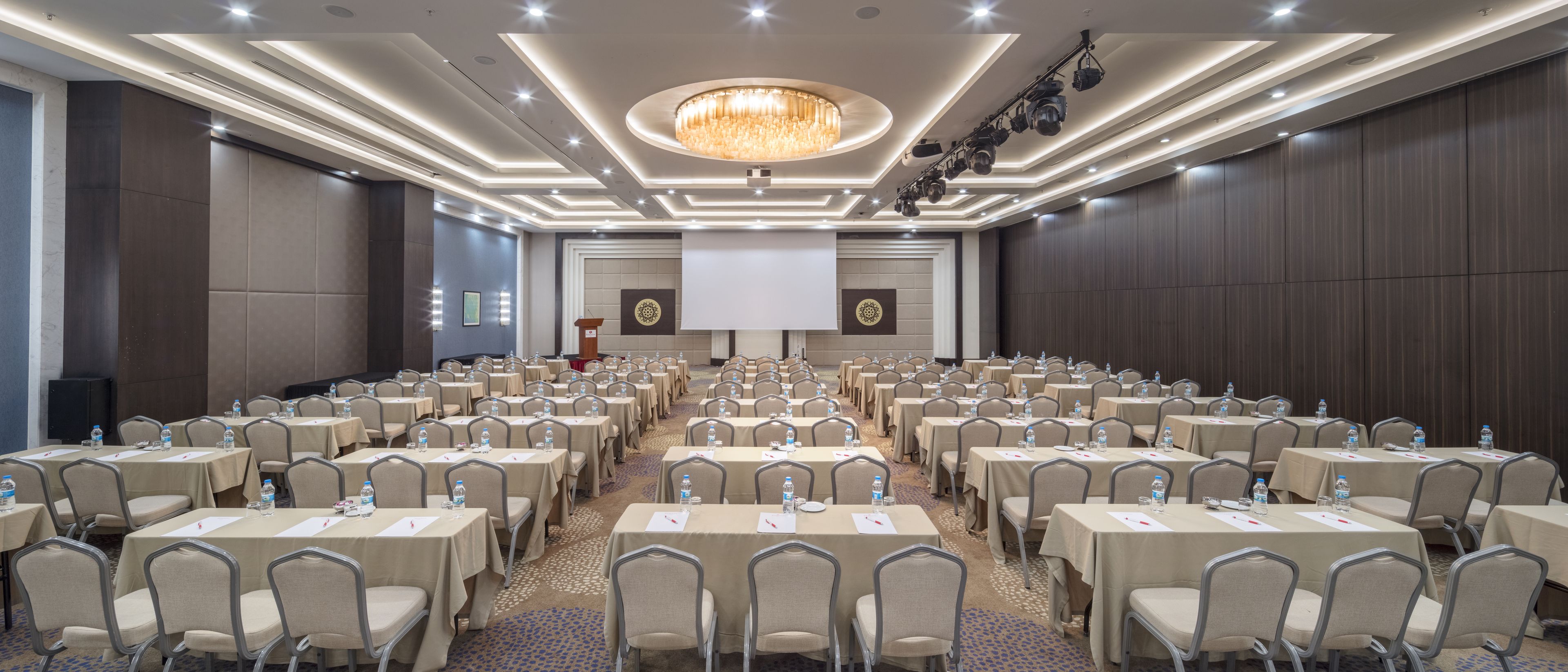 A conference room with rows of tables and chairs, a large screen, and a podium.