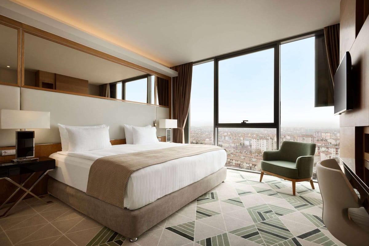 Une chambre d’hôtel avec un grand lit, une chaise, une télévision et une vue sur la ville.