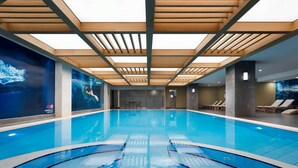 Une piscine intérieure à l’eau claire, avec des poutres en bois au plafond et une fresque murale.