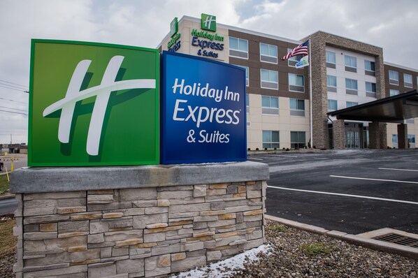 Een Holiday Inn Express & Suites bord met een stenen voet, voor een gebouw met meerdere ramen en een Amerikaanse vlag.