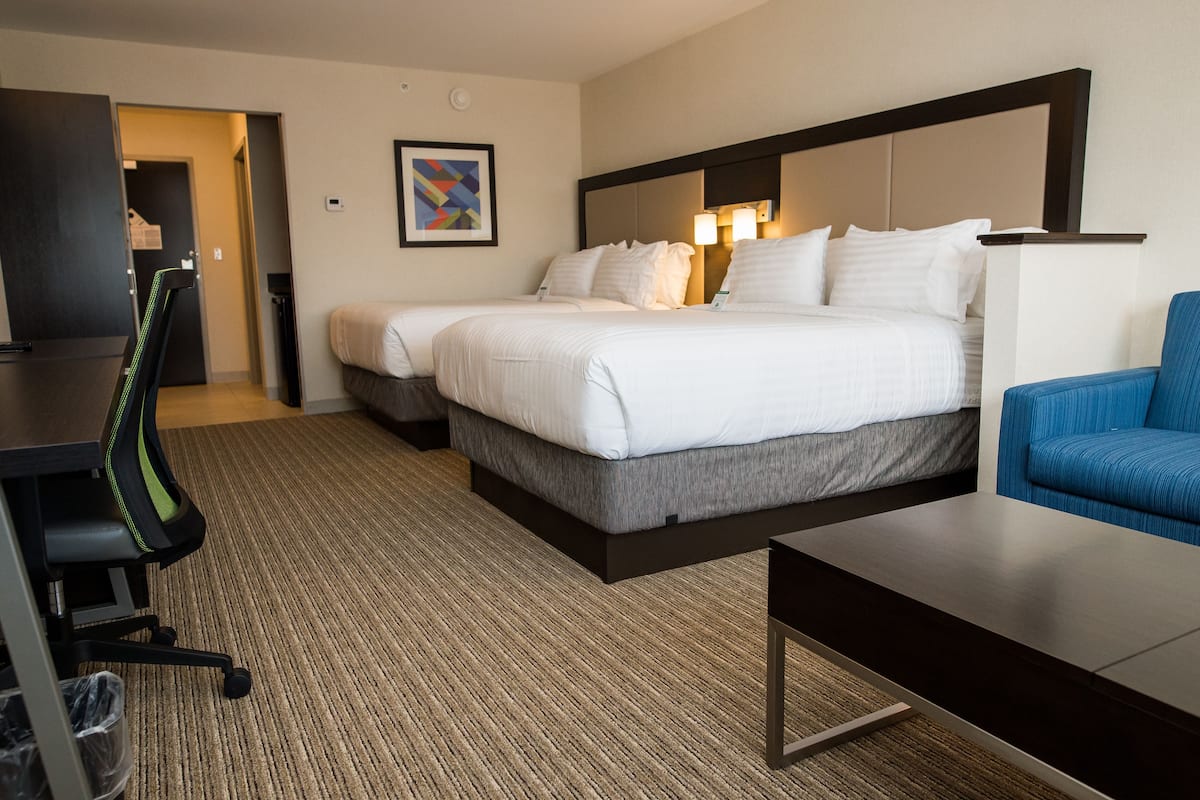 A hotel room with two beds, a desk, a chair, and a carpeted floor.