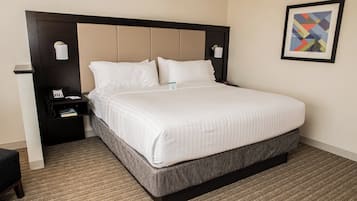 A hotel room with a large bed, a nightstand, a wall-mounted lamp, and a framed picture.