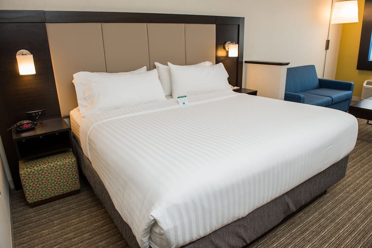 A hotel room with a large bed, a nightstand, a chair, and a lamp.