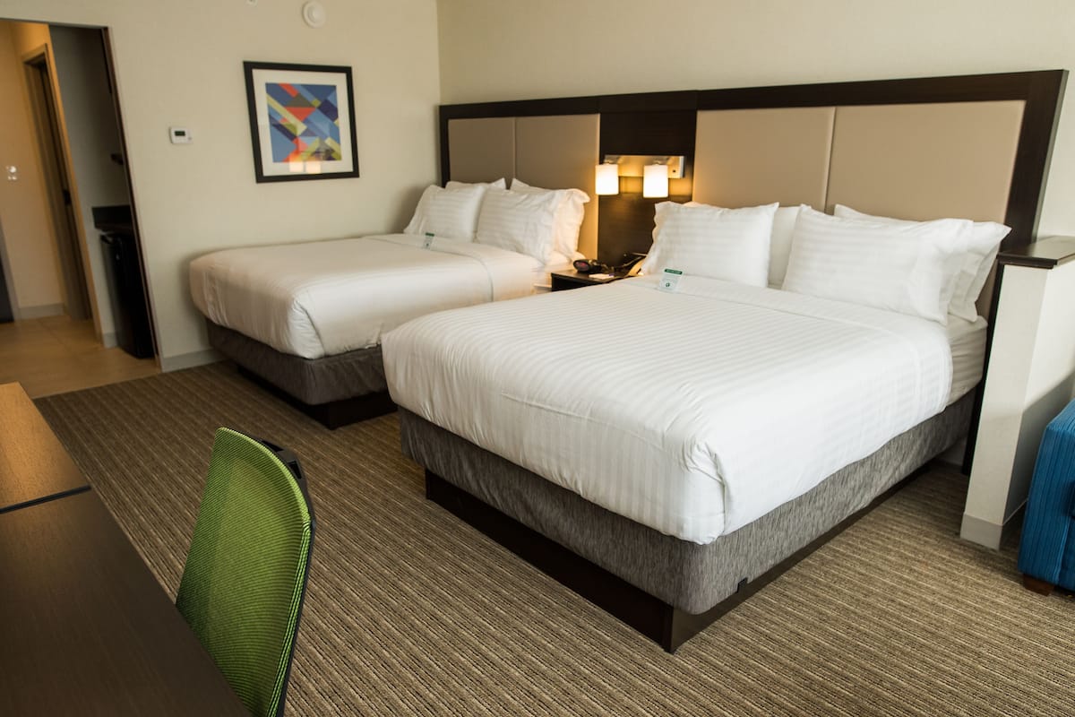 A hotel room with two single beds, a desk, a chair, and a nightstand with a lamp.