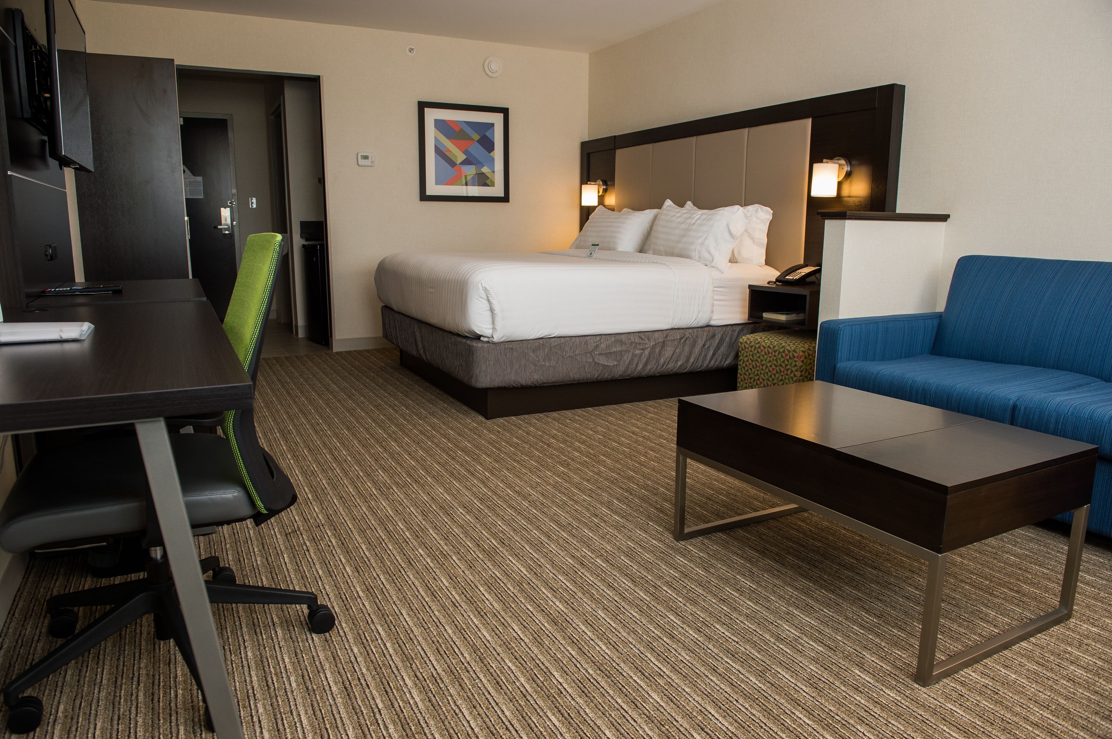 A hotel room with a bed, a desk, a chair, a couch, and a carpeted floor.