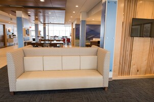Un moderno vestíbulo de hotel con una zona de estar central, un mostrador de recepción y un comedor al fondo.