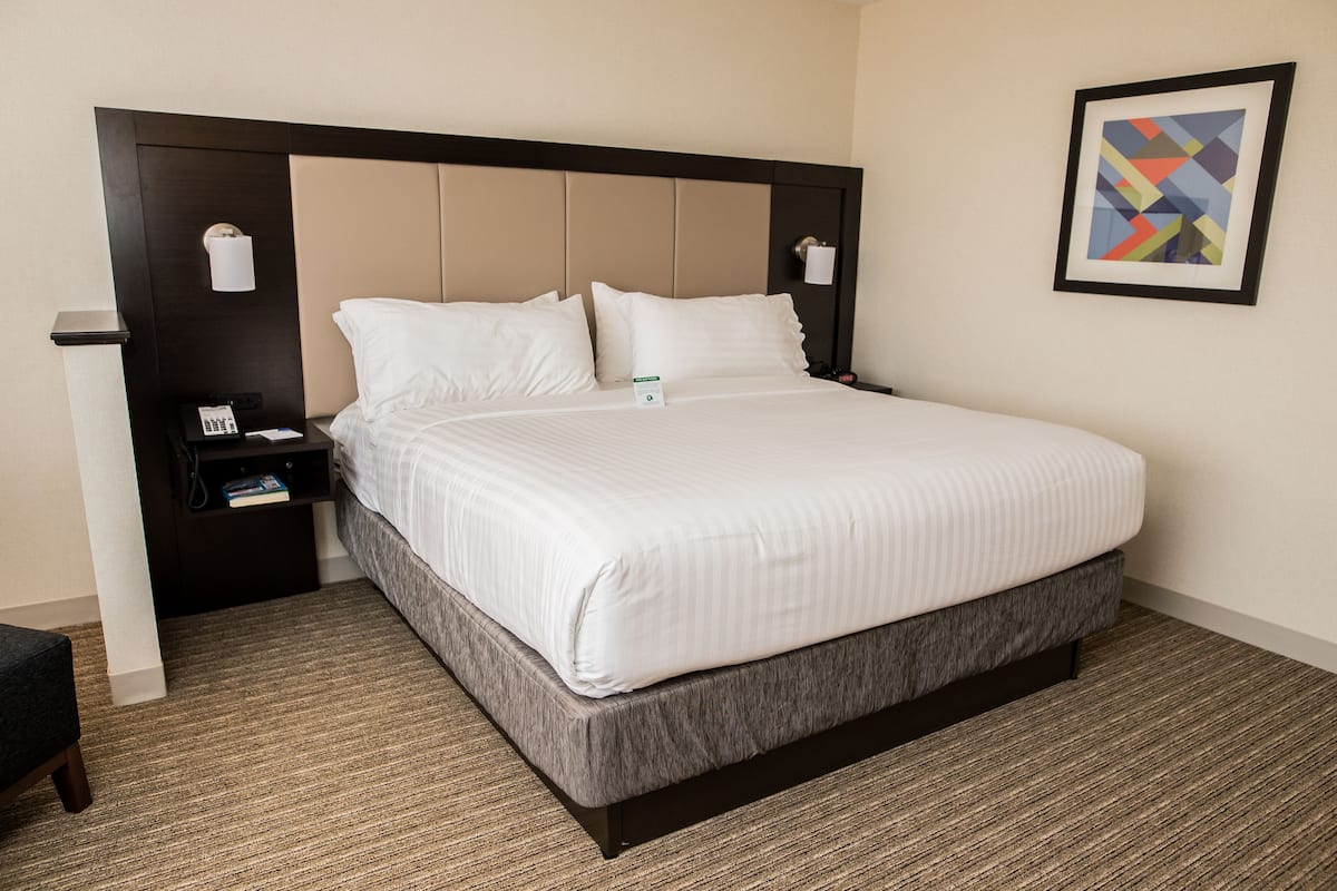 A hotel room with a large bed, a nightstand with a phone and a lamp, and a framed picture on the wall.