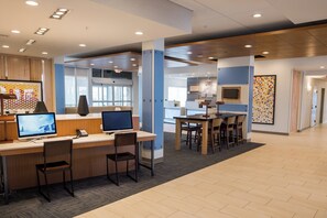 A modern office space with desks, chairs, and computers. There is a reception area with a counter and a large window.