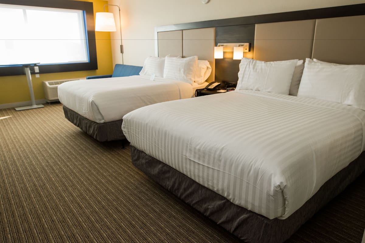 A hotel room with two beds, a flat-screen TV, and a bedside table with a lamp.