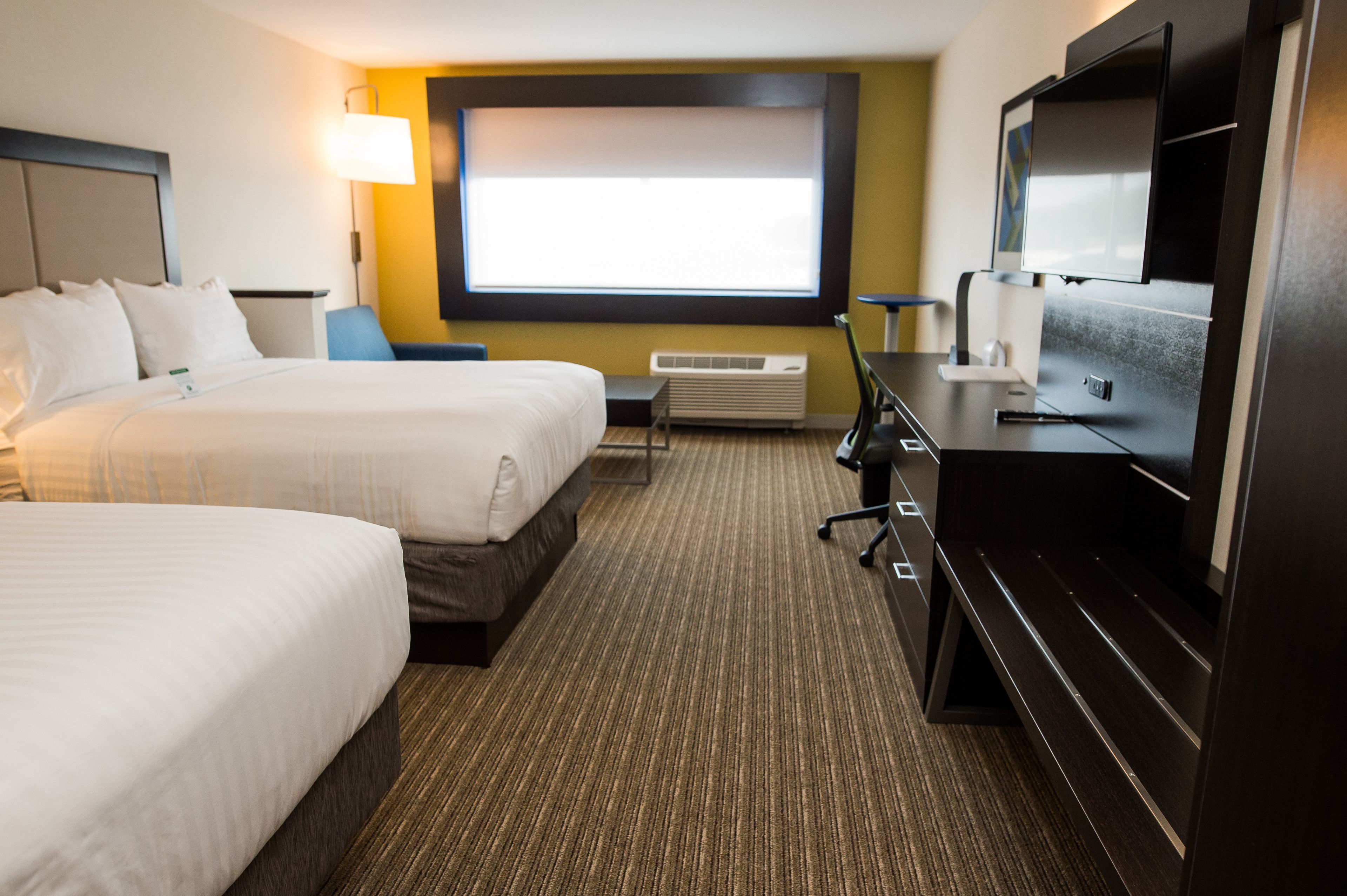 A hotel room with two beds, a desk, a flat-screen TV, and a large window.