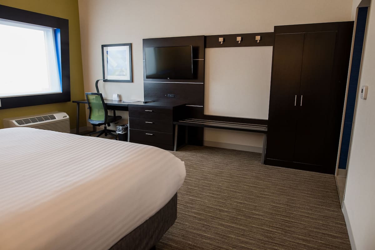 A hotel room with a large bed, a desk with a computer, a TV, and a wardrobe.