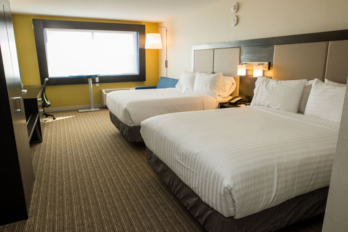 A hotel room with two beds, a desk, a chair, and a large window.
