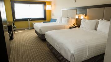 A hotel room with two beds, a desk, a chair, and a large window.