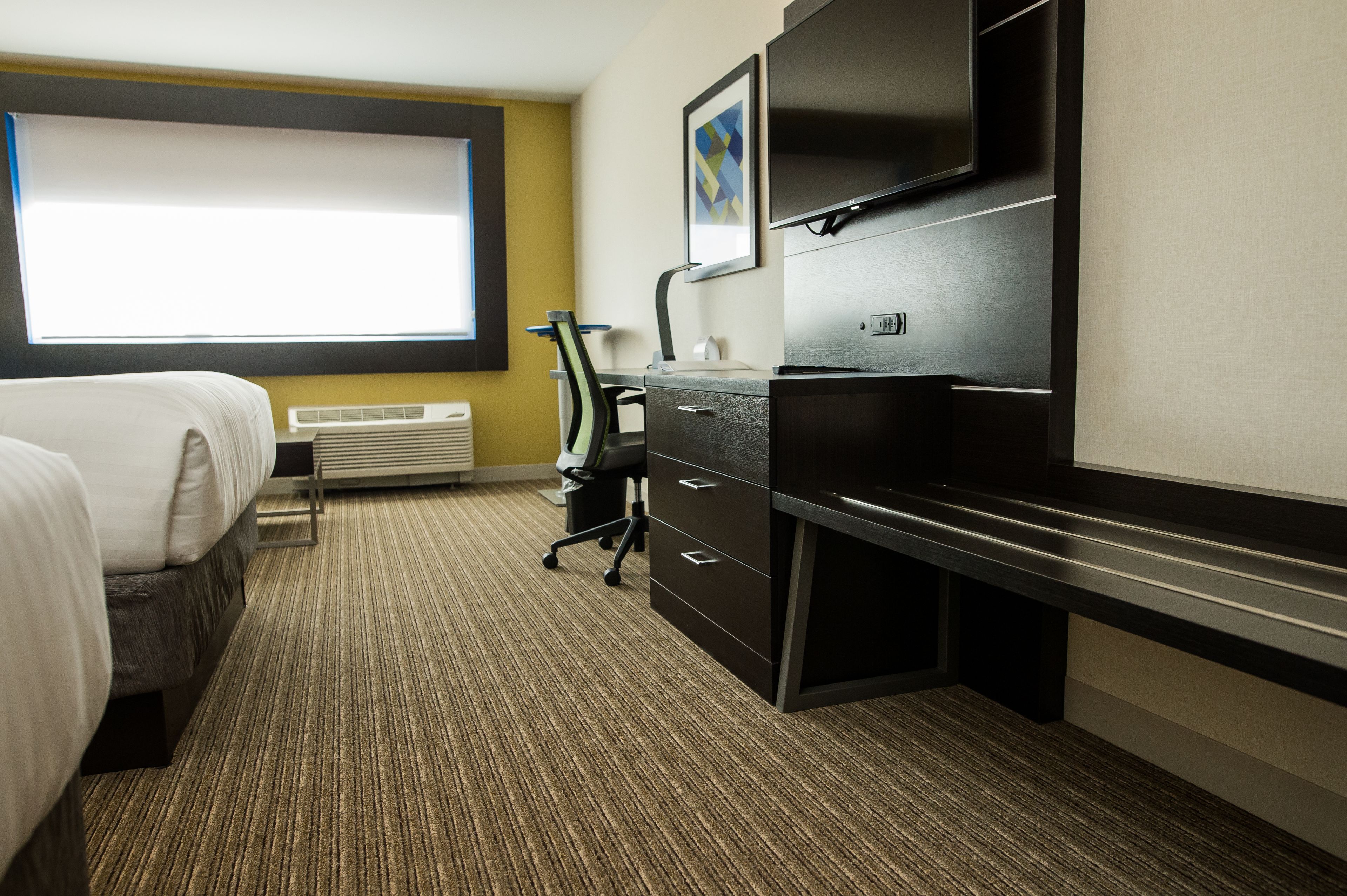 A hotel room with a bed, desk, chair, and a large window.