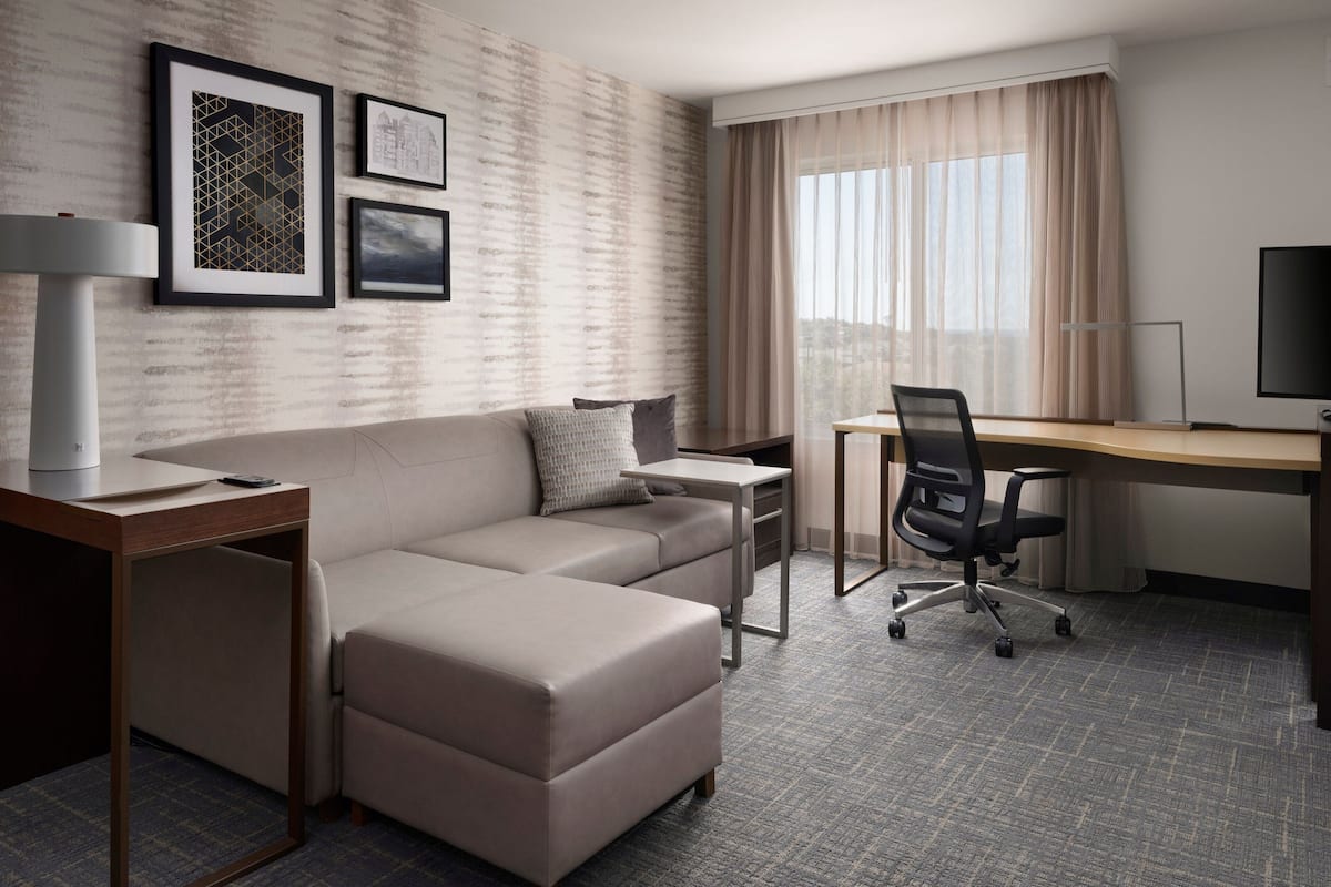 A modern hotel room with a beige sofa, a desk, a chair, and a TV.