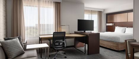 Quarto de hotel com cama, escrivaninha, televisão, sofá e poltrona.