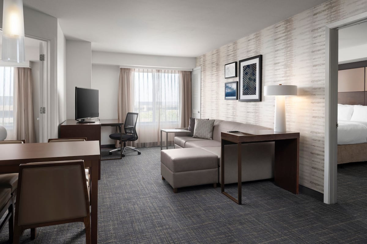 A hotel room with a bed, a desk, a chair, a sofa, and a television.