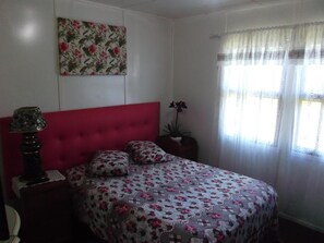 A bedroom with a red headboard, floral bedspread, and a single potted plant. - Pousada Roses Canela (Canela)