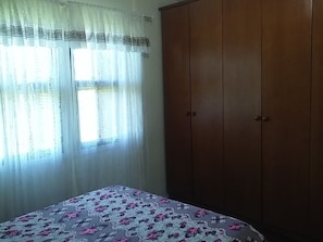 Un dormitori amb llit, armari i finestra amb cortines de tela fina.