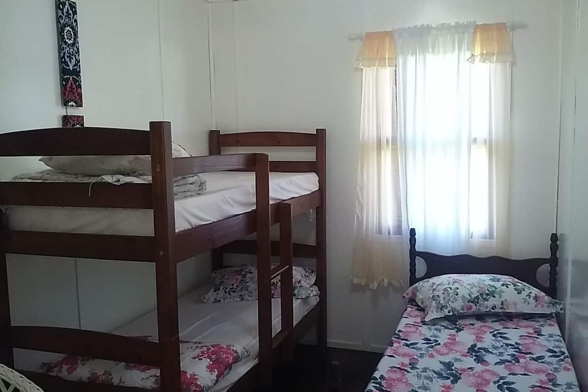 A bunk bed room with a single bed and a window with curtains.