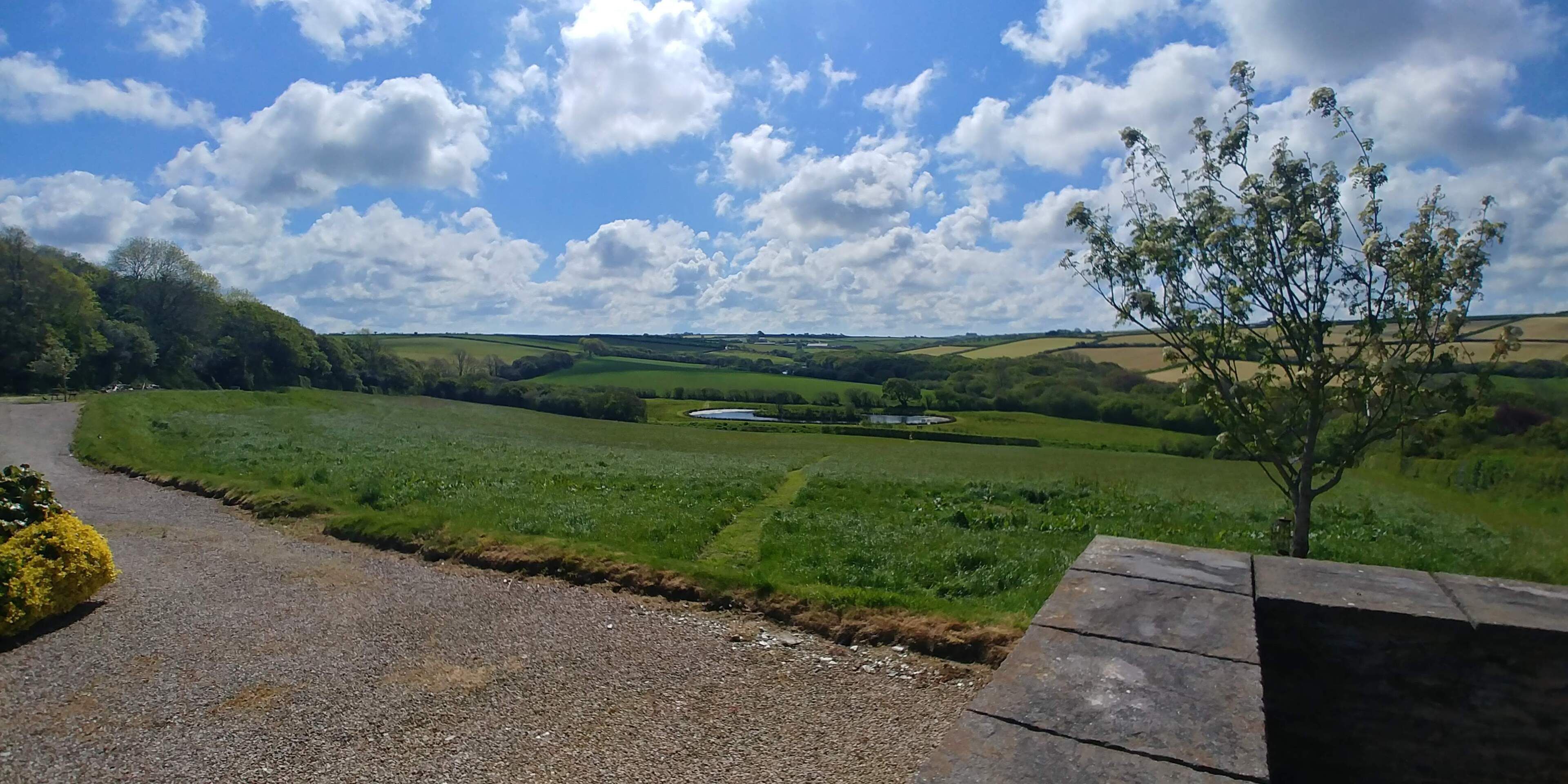 Un paysage rural avec un chemin de gravier, des champs verdoyants et une étendue d’eau.