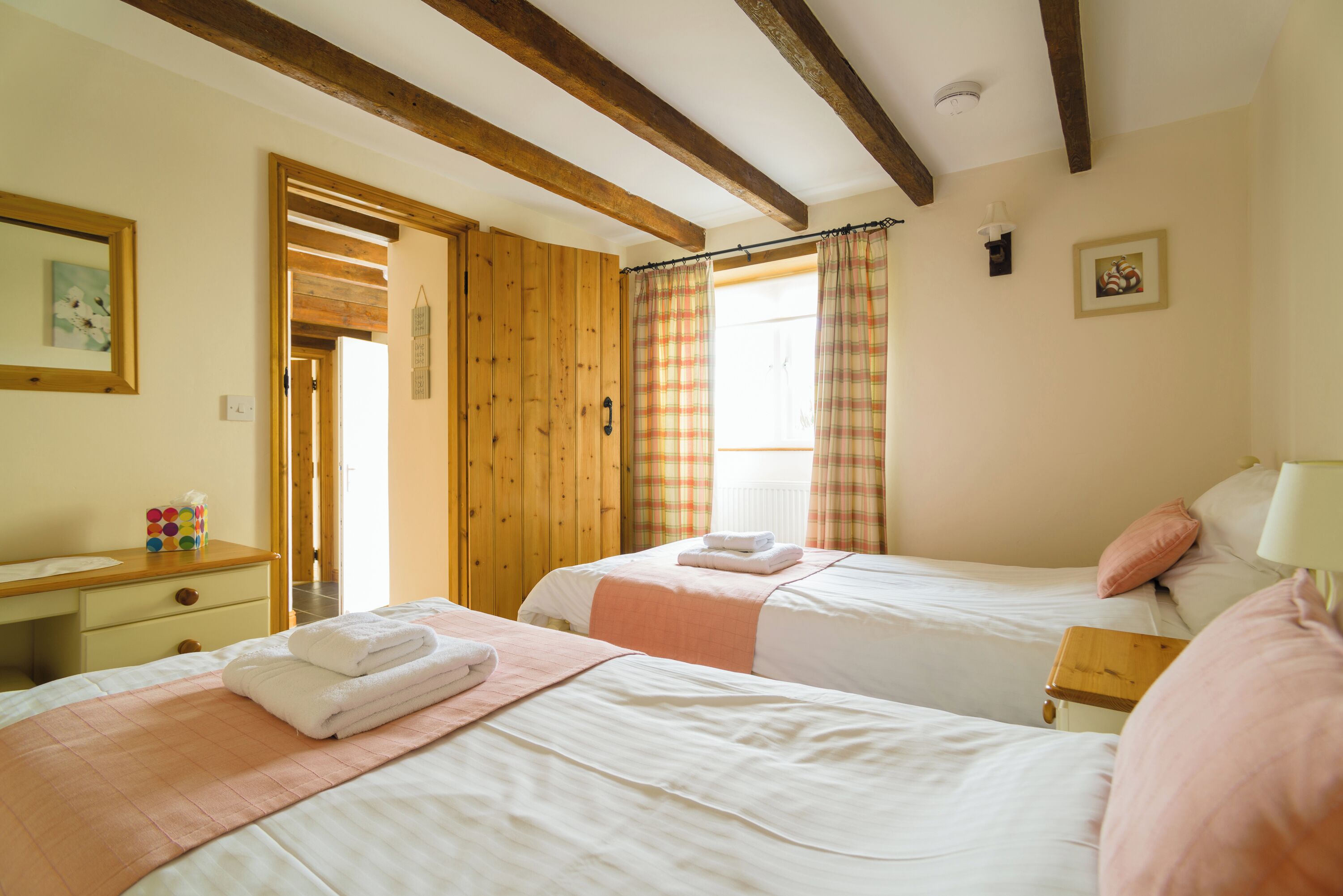 Une chambre avec deux lits, des poutres en bois, un bureau avec une chaise et une fenêtre avec des rideaux.