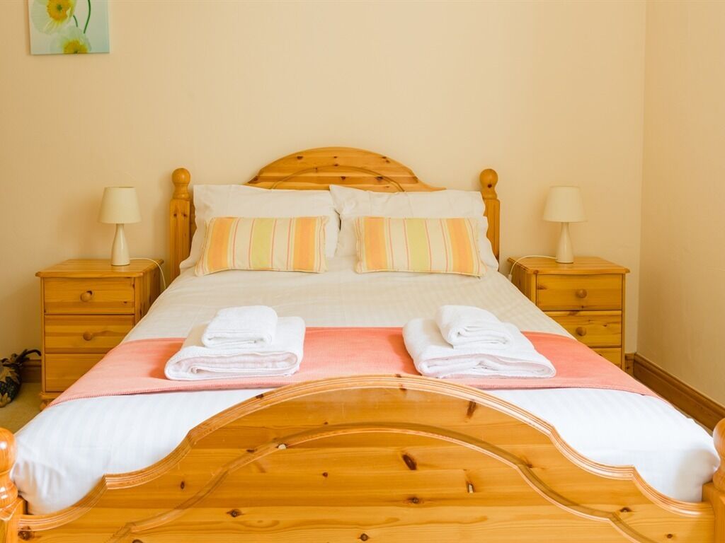 A single bed with a wooden headboard, two bedside tables with lamps, and a pink bedspread.