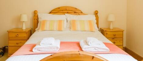 A single bed with a wooden headboard, two bedside tables with lamps, and a pink bedspread.