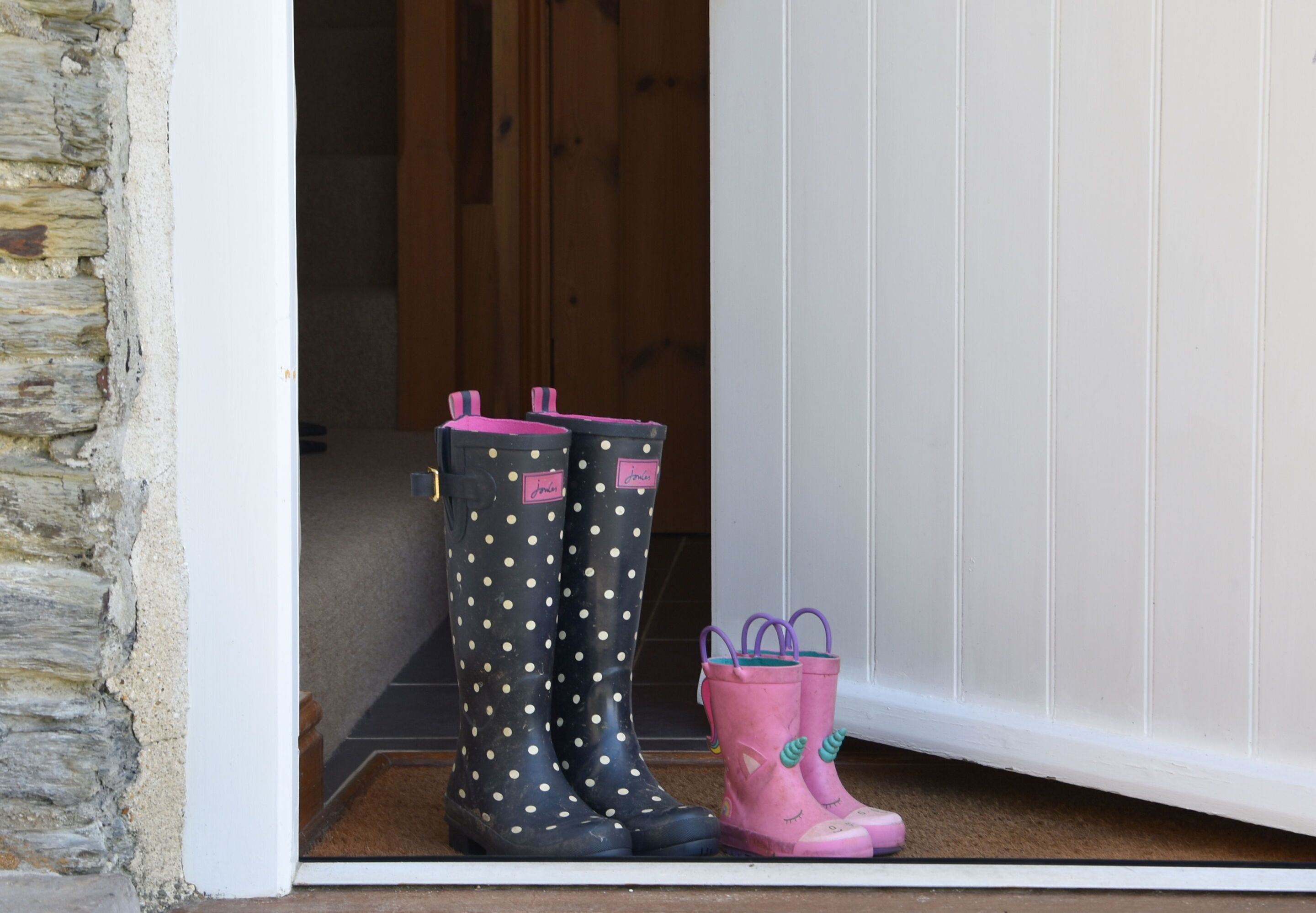 A set of black and pink rain boots on a white door threshold.