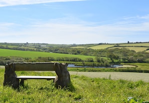 A bench in a grassy field with a view of rolling hills and a body of water in the distance. - Degembris Cottages (Newquay)