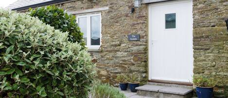 A stone building with a white door and a window. There are potted plants outside.