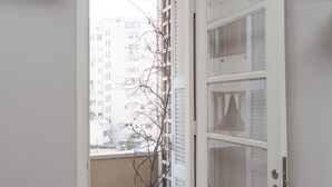 Un pasillo estrecho con una planta en maceta, una puerta blanca con paneles de vidrio y un aire acondicionado instalado.