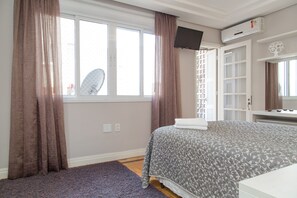 A bedroom with a bed, a window with curtains, an air conditioning unit, and a television mounted on the wall. - Apartamento Redenção (Porto Alegre)